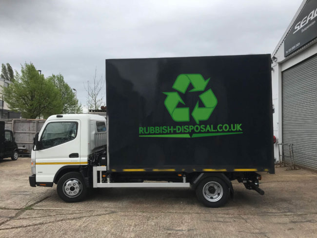 Black-with-logo Rubbish Disposal lorry from side on view point