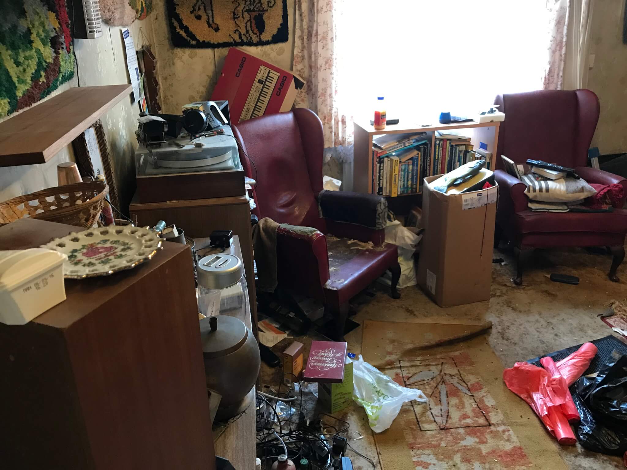 Living room with broken red chair and rubbish on the floor