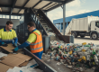 Workers sorting recyclable materials such as cardboard, plastic, and metal at a modern waste recycling facility in Brentwood with a collection truck in the background